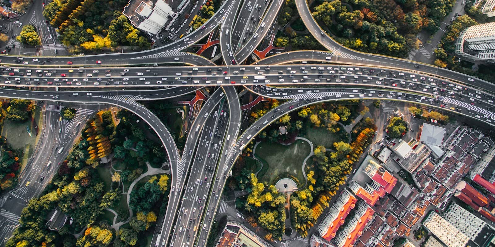 Flyfoto av et stort motorveikryss der rampene svinger mellom trær og hustak