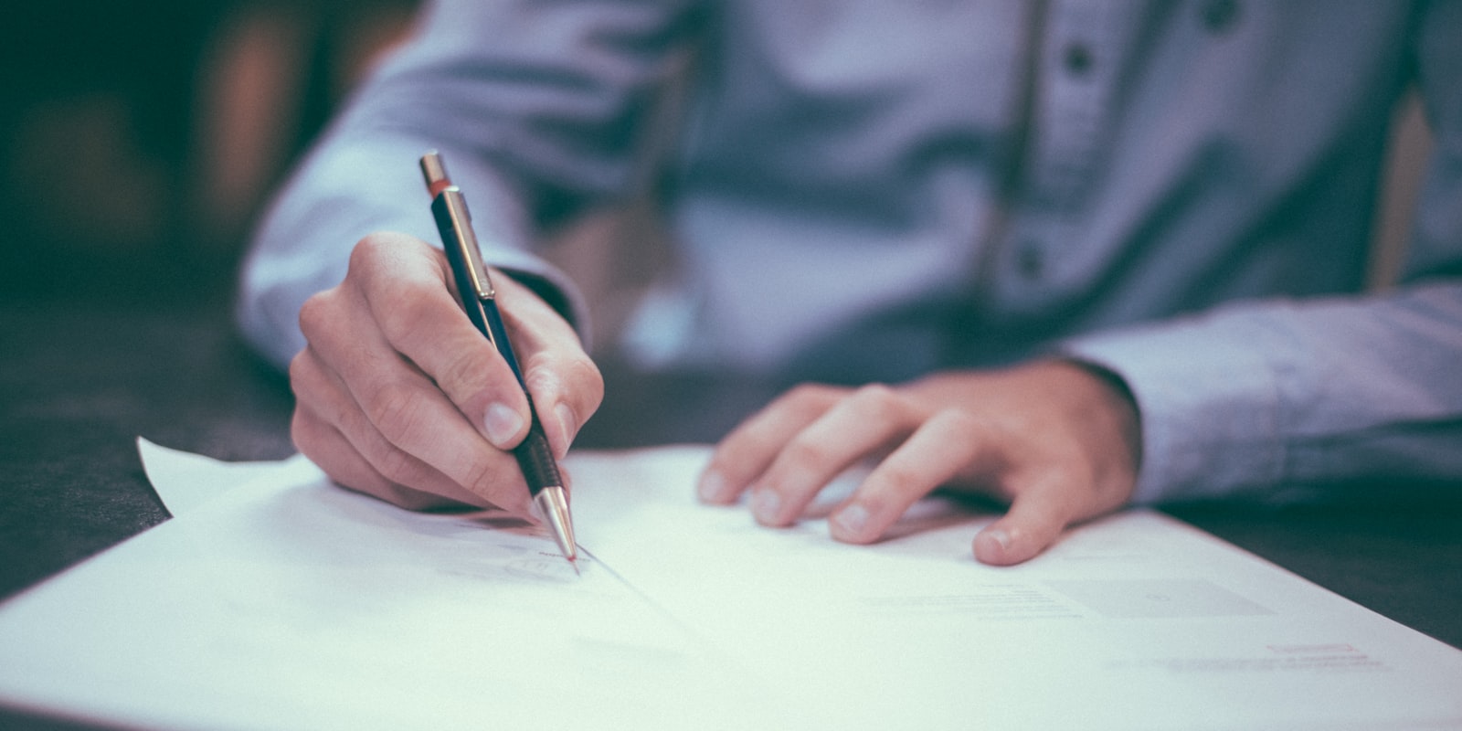 En person som leser gjennom og signerer et dokument ved et skrivebord