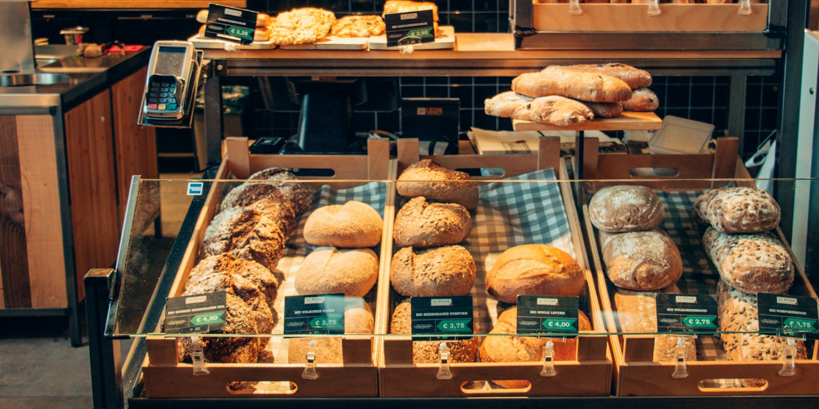En bakeridisk med ferske brød og rundstykker i trekasser, med en prislapp foran hver kasse
